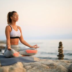 young-woman-practicing-yoga-relaxation-exercises-meditating-rock-beach-copy-space